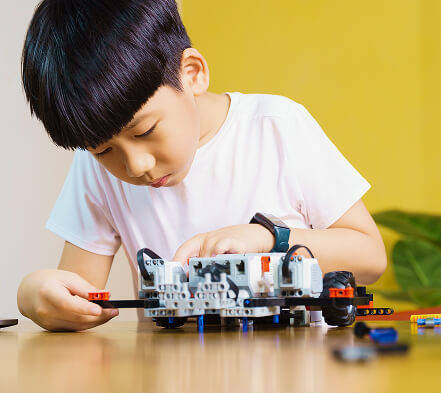 Focused child assembling a robotics project, illustrating enrichment programs such as coding, robotics, AI, and art that nurture creativity and future-ready skills.
